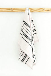 A white kitchen towel with navy diagonal stripes hanging from a light wood dowel against a plain white wall.