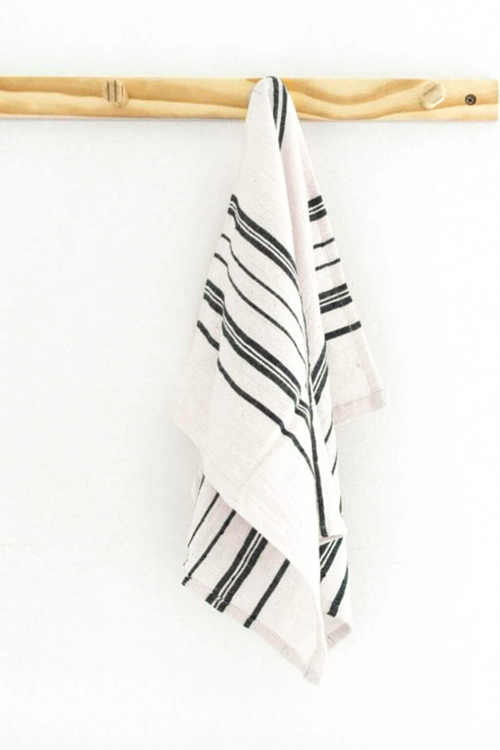 A white kitchen towel with navy diagonal stripes hanging from a light wood dowel against a plain white wall.