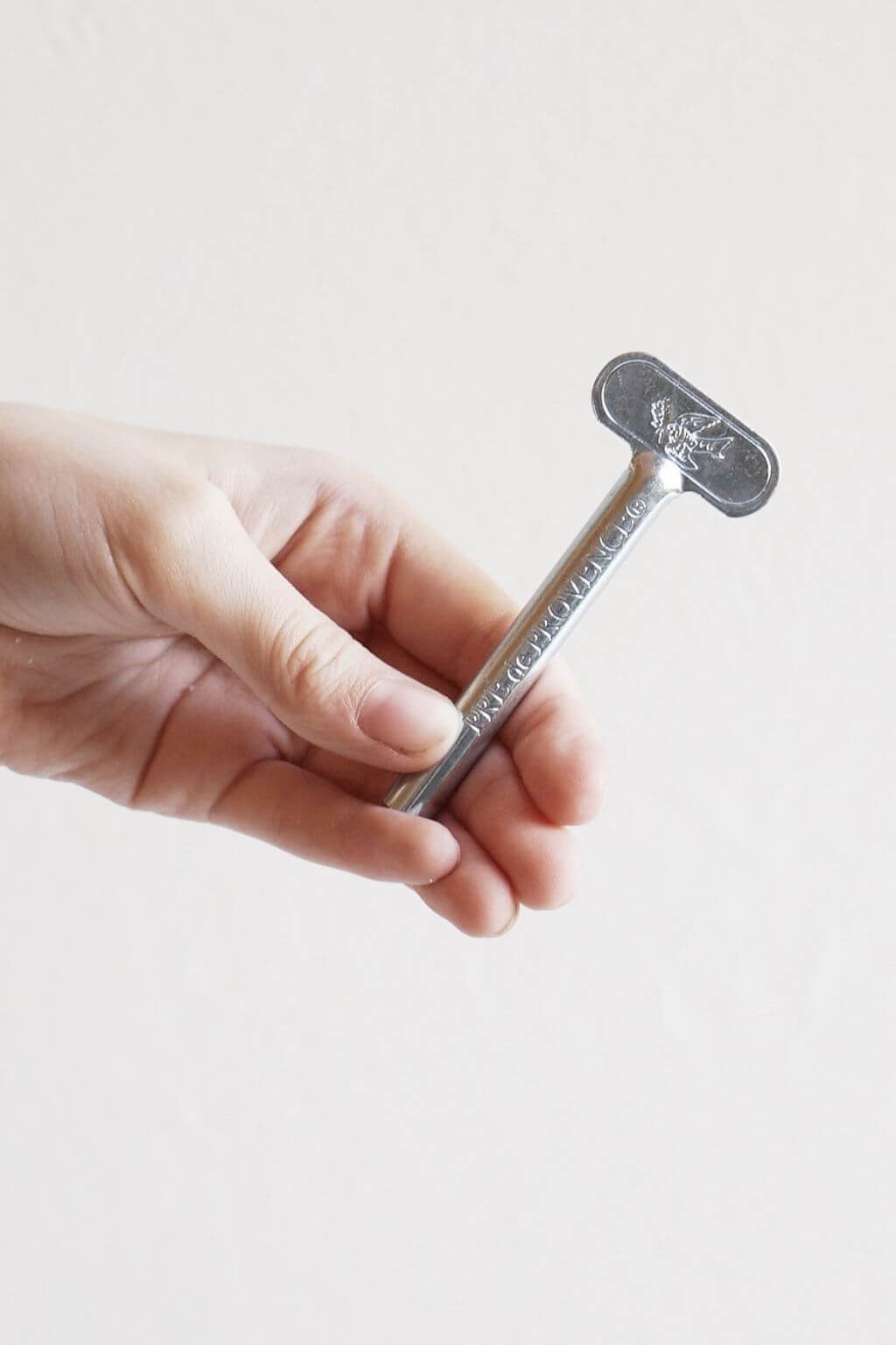 Close-up of a hand holding a silver Metal Tube Roller Key against a light neutral background, highlighting its simple, durable design.