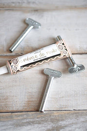 Metal Tube Roller Keys displayed on a rustic wooden surface, one inserted into a decorative cream tube to neatly roll it closed.