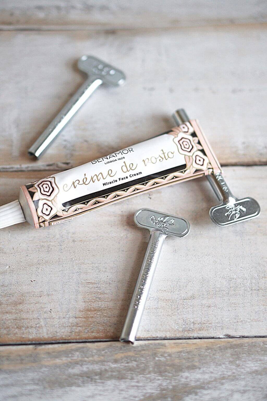 Metal Tube Roller Keys displayed on a rustic wooden surface, one inserted into a decorative cream tube to neatly roll it closed.