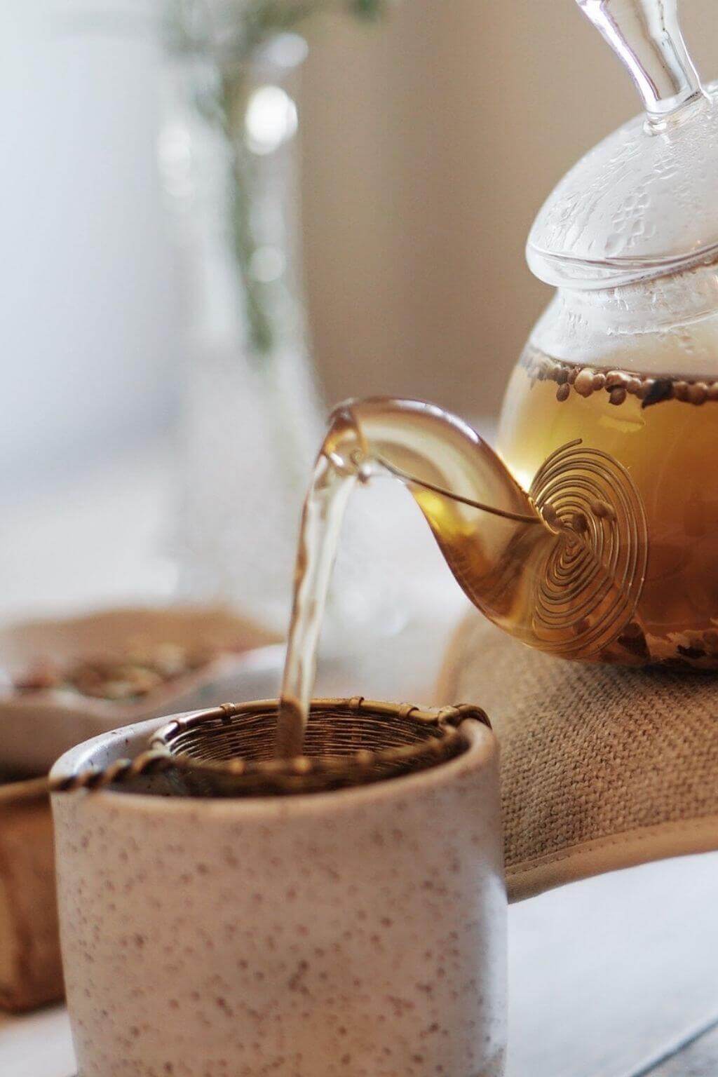 Close-up of woven raw brass tea infuser in a ceramic teacup with tea being poured into the strainer