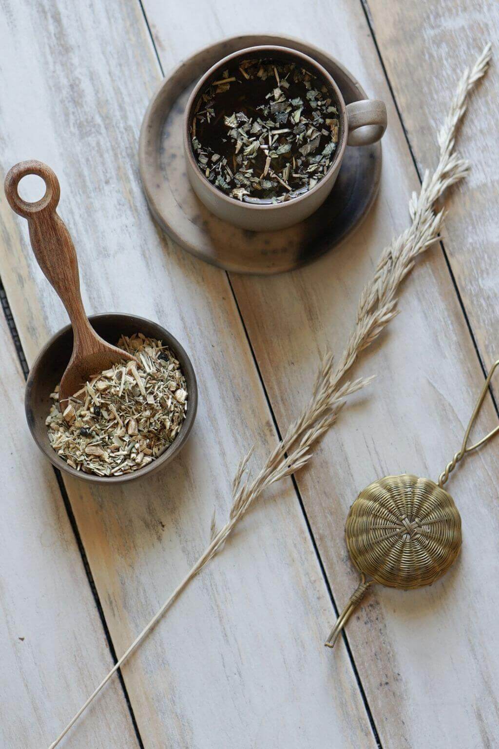 Brass tea strainer resting beside a handmade ceramic mug
