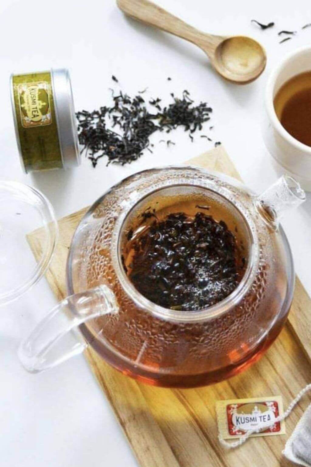 Top view of all glass teapot with infuser basket brewing tea on a wood cutting board with tea accesssories nearby
