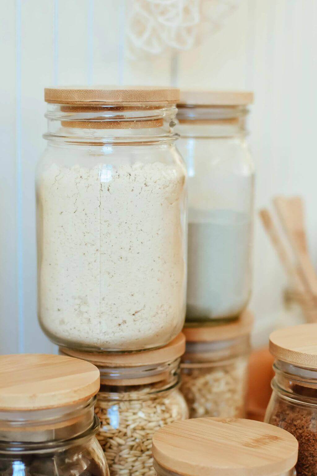 Glass jars with bamboo lids containing various dry goods on a white background